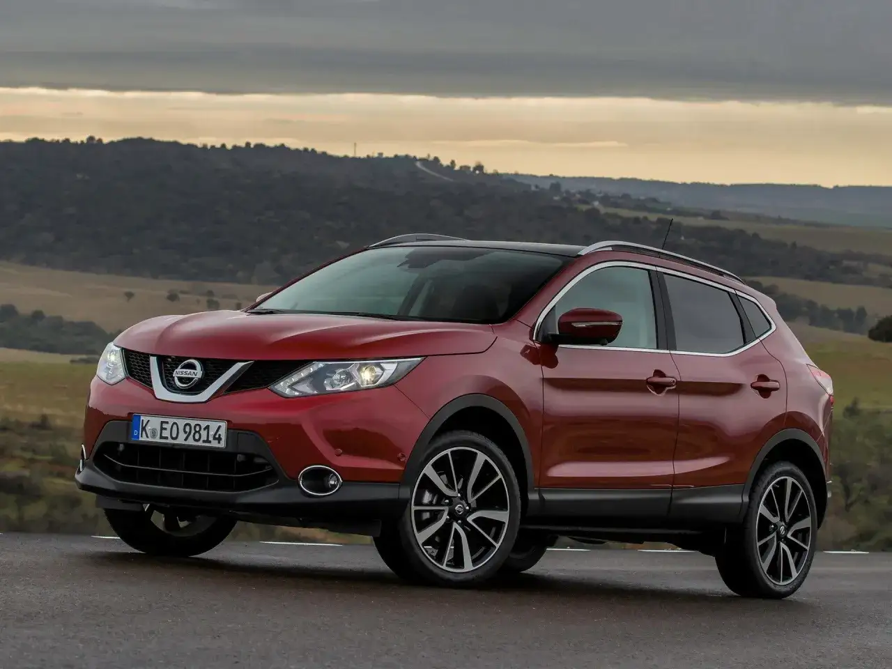 Czerwony Nissan Qashqai 1.2 benzyna na tle krajobrazu. Wiele osób szuka opinii o tym modelu.