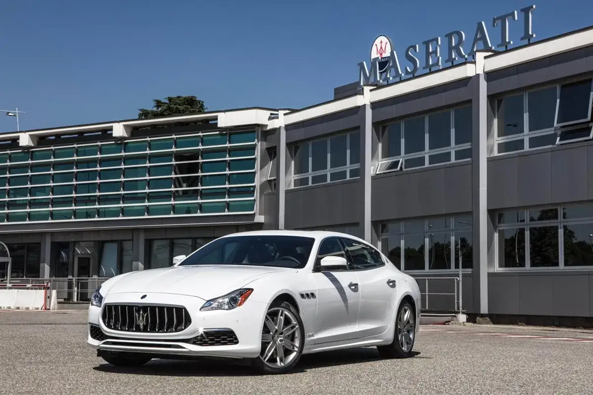 Białe Maserati Quattroporte przed budynkiem Maserati. Nawet luksusowe auta miewają maserati quattroporte awarie i problemy.