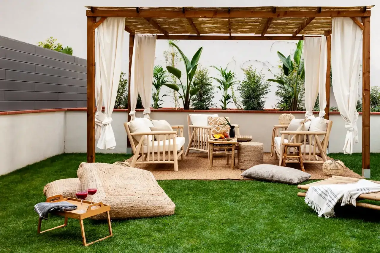 Ideas para terrazas con césped artificial: un rincón acogedor bajo pérgola de bambú, con muebles de madera clara y cojines.