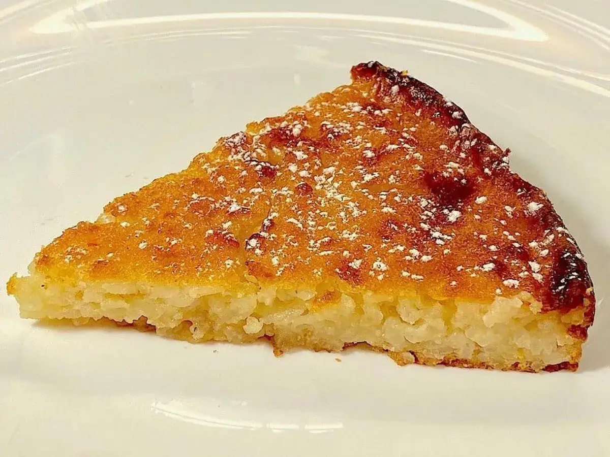 Una fetta di torta di riso, dorata e cosparsa di zucchero a velo. Un classico profumo di torta di riso ricetta della nonna.