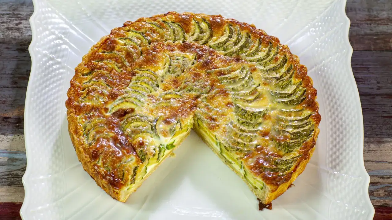 Torta salata con zucchine, dorata e invitante, con fette di zucchine disposte a raggiera e formaggio fuso.
