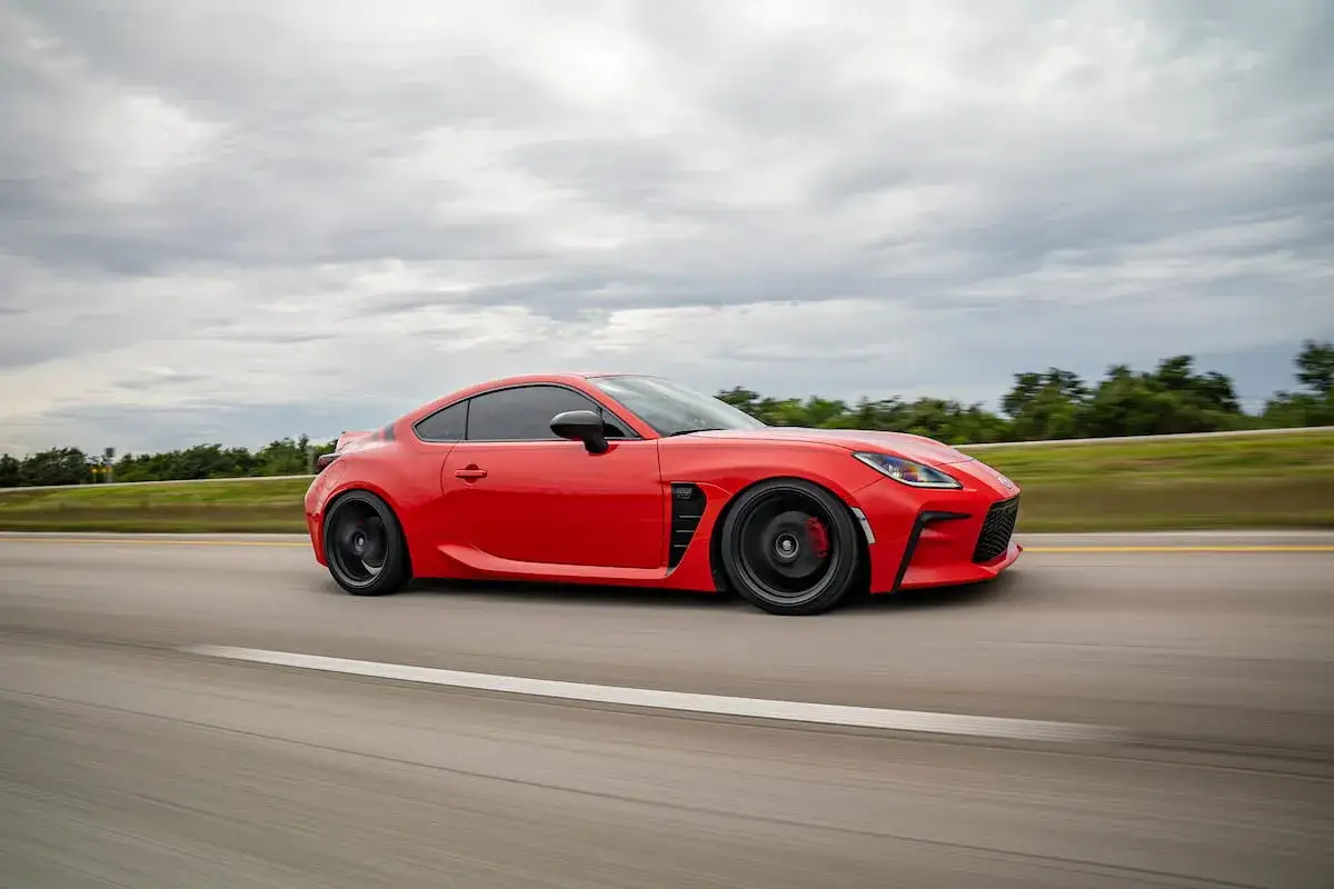 Un deportivo rojo, que es un coche coupe, acelera por una carretera con un cielo nublado.