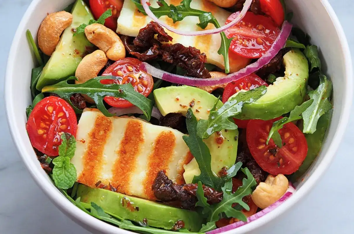 Pyszna sałatka z grillowanym halloumi, awokado, pomidorkami, rukolą i orzechami nerkowca.