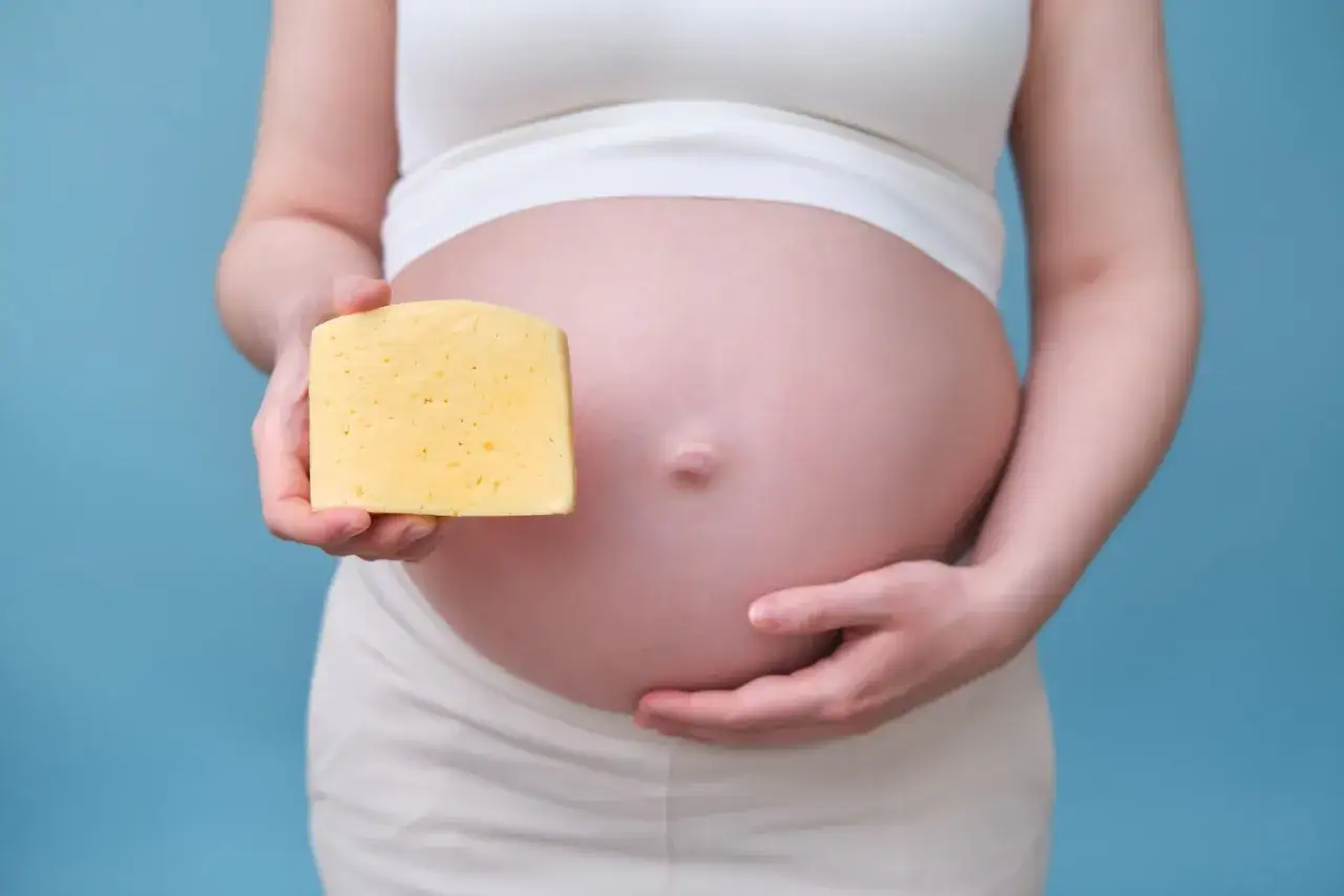 Schwangere h&auml;lt ein St&uuml;ck Mozzarella vor ihrem Bauch.