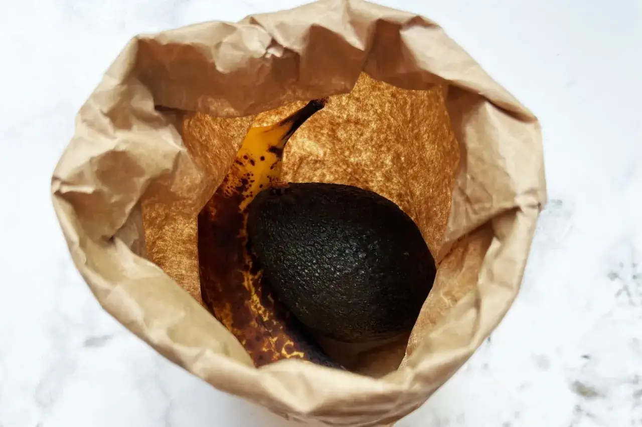 Eine Banane hilft, die Avocado reifen zu lassen. Beide liegen in einer braunen Papiertüte.