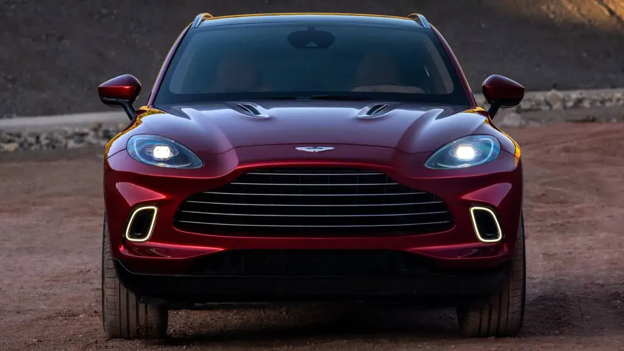 Czerwony Aston Martin DBX, najładniejszy SUV, z charakterystycznym grillem i światłami LED, stoi na pustynnym podłożu.
