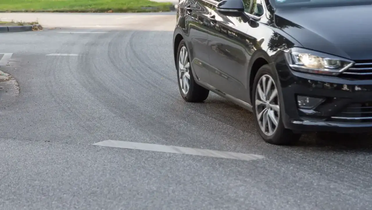 Schwarzes Auto fährt eine Kurve, die Reifen quietschen beim Beschleunigen.
