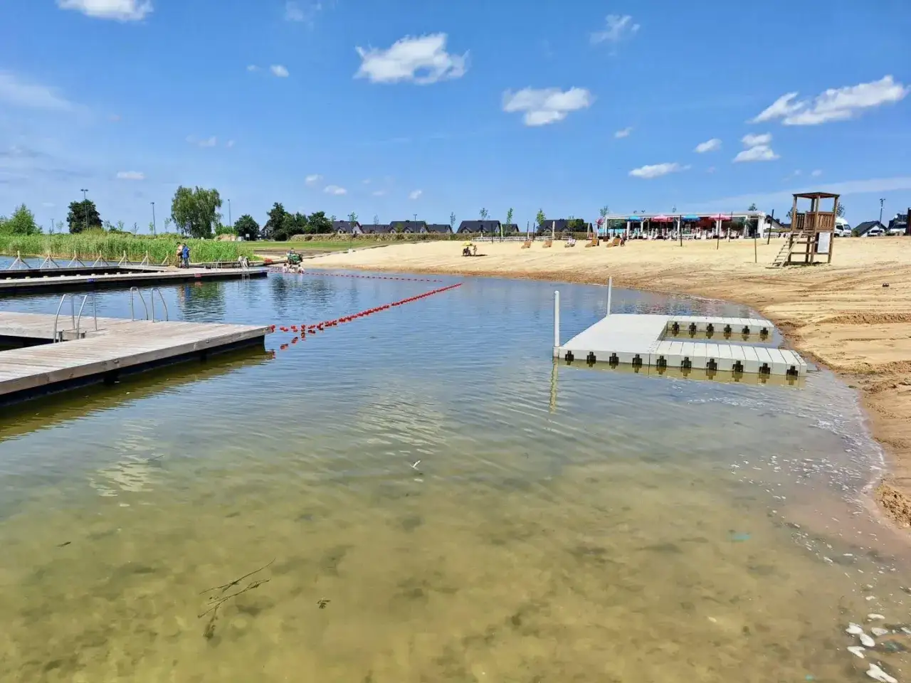 Sieraków jezioro atrakcje: drewniane pomosty, piaszczysta plaża, ratownik na wieży, pływający pomost i czerwona lina wyznaczająca kąpielisko.
