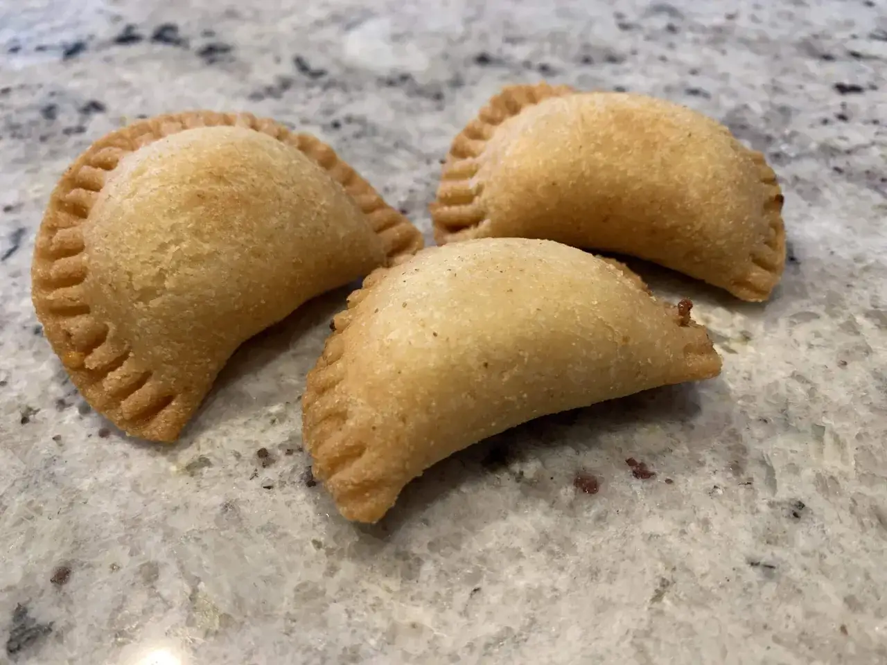 Trois samboussek fromage dor&eacute;s, pr&ecirc;ts &agrave; &ecirc;tre d&eacute;gust&eacute;s, sur un plan de travail marbr&eacute;.