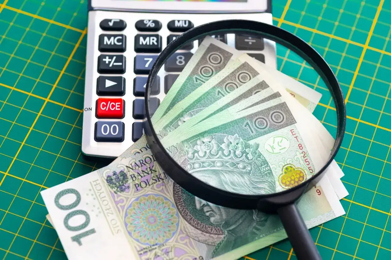 Kalkulator i lupa badają banknoty 100 zł. Zastanawiasz się, ile wynosi podatek belki?