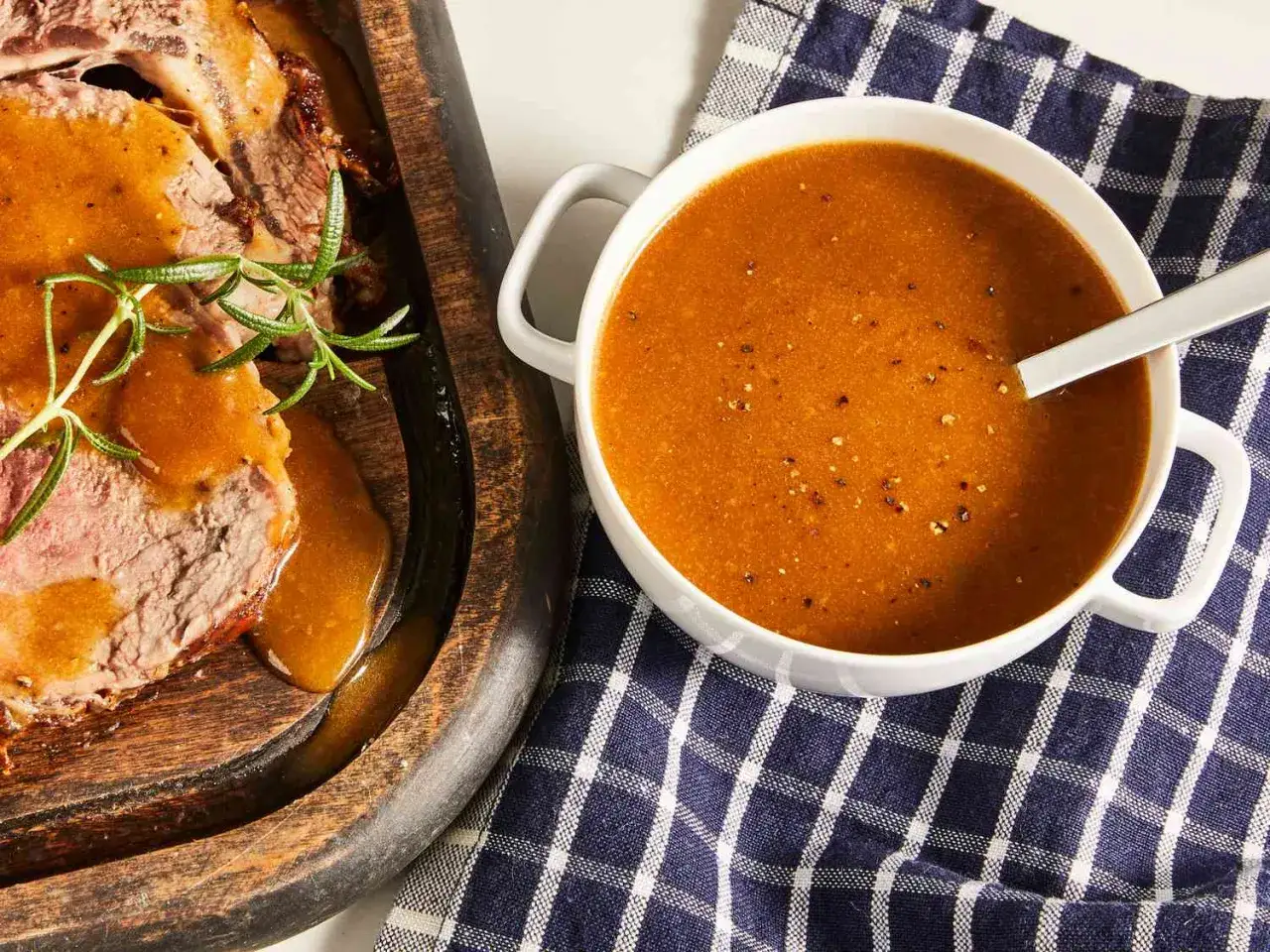Tranches de rôti de bœuf arrosées d'un riche jus de viande, accompagnées d'une sauce onctueuse dans un bol.