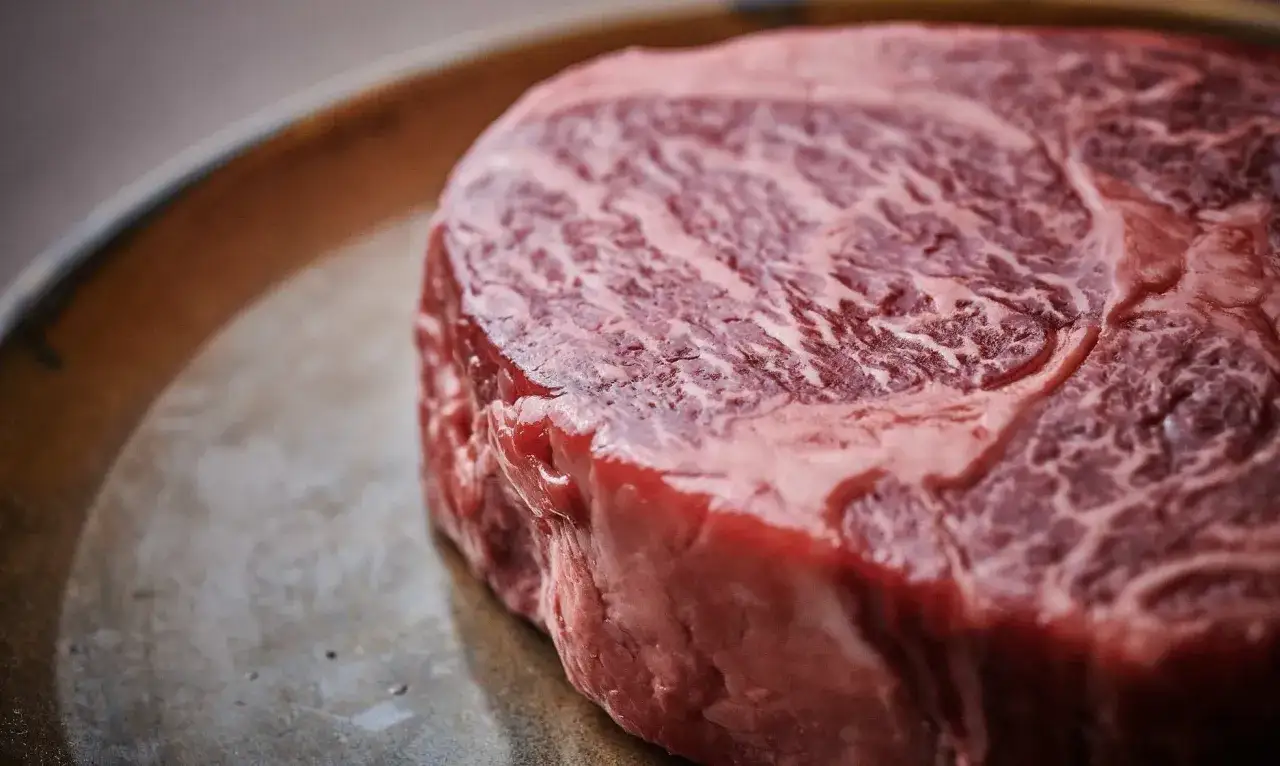 Un jugoso ojo de bife crudo, con su marmoleado caracter&iacute;stico, descansa sobre un plato met&aacute;lico, listo para ser cocinado.