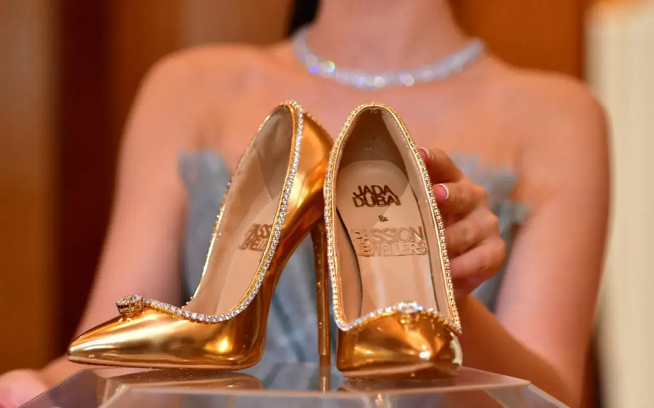 Złote szpilki wysadzane diamentami, ozdobione logo Jada Dubai. Prawdopodobnie najdroższe buty na świecie, prezentowane przez kobietę w błyszczącym naszyjniku.