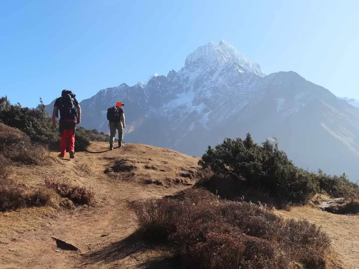 Dw&oacute;ch turyst&oacute;w wyrusza na trekking w Himalajach. Przed nimi majestatyczny, ośnieżony szczyt.