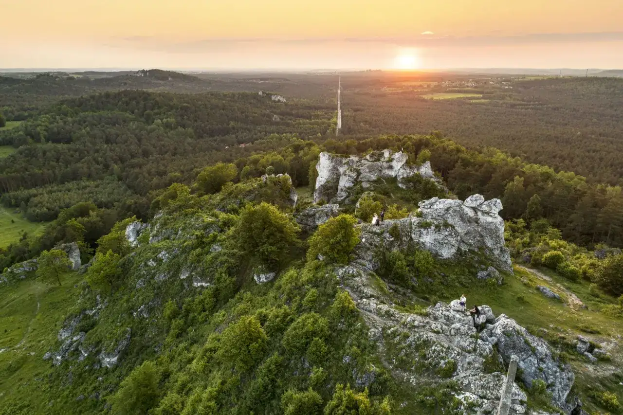Malowniczy krajobraz z wapiennymi skałami i lasem. Na szczycie góry zborów trasa dla turystów, a w oddali zachodzące słońce.
