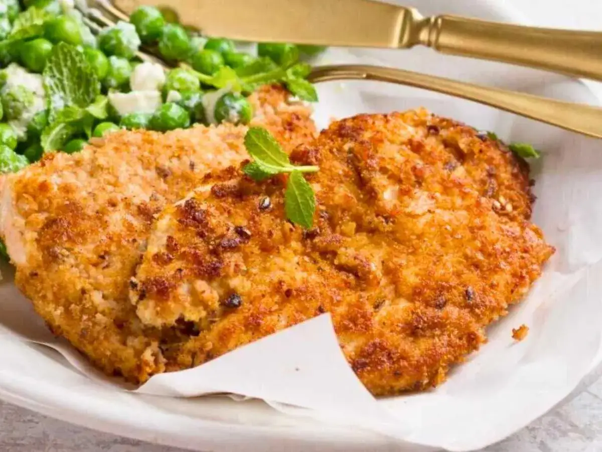 Dos milanesas de pollo doradas y crujientes, servidas con una ensalada de guisantes frescos y menta.