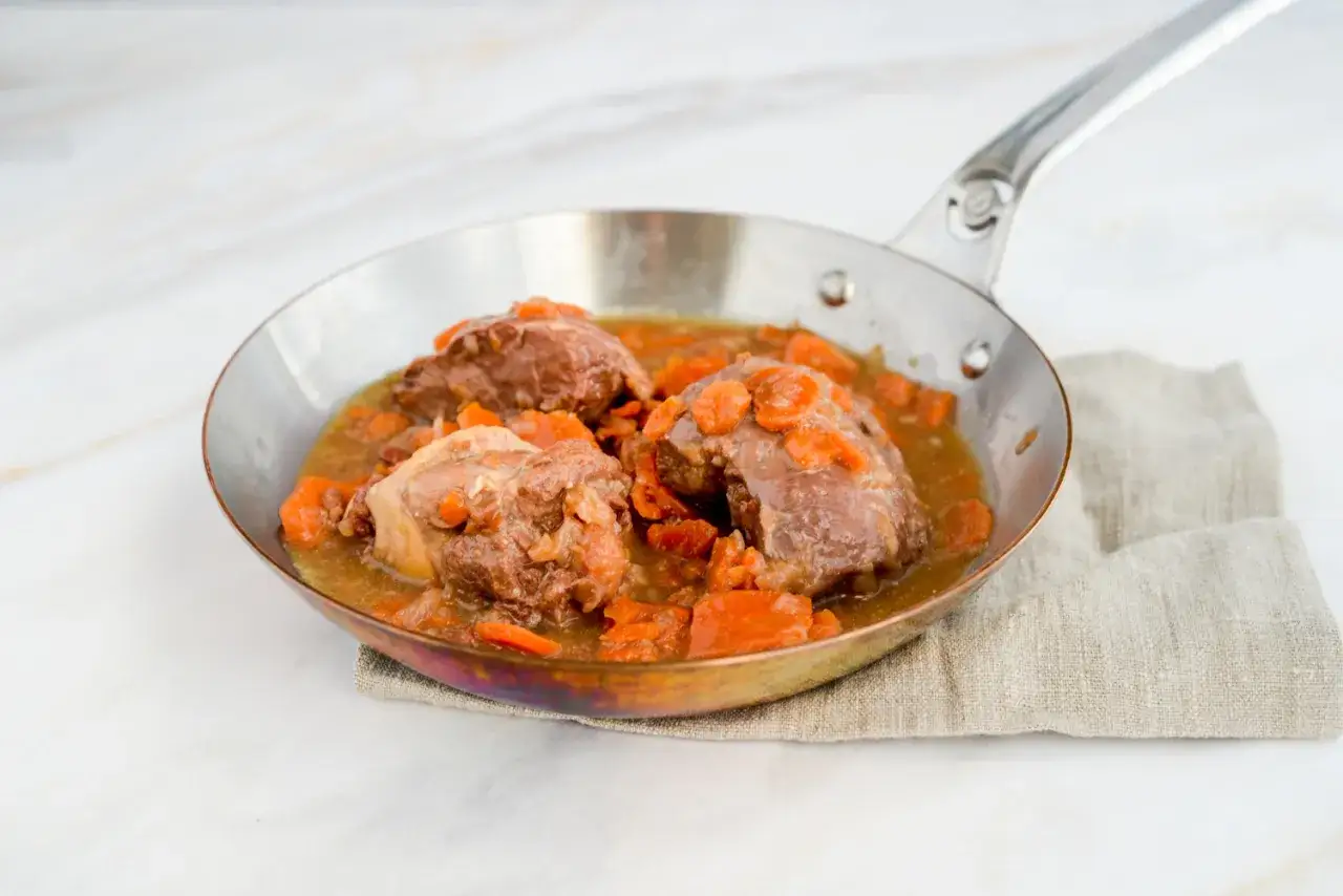 Herzhaftes Daube Proven&ccedil;ale in einer Pfanne mit Karotten und Sauce, serviert auf einem Leinentuch.