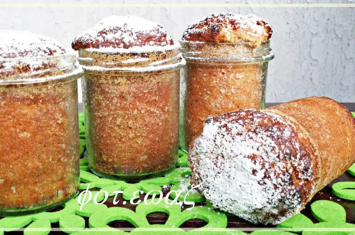Babka w słoiku, posypana cukrem pudrem, wygląda apetycznie. Obok leży kolejna babka, jakby gotowa do podania.