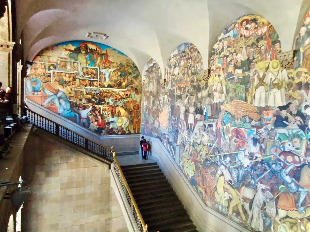 Vibrant murals depicting historical scenes line a grand staircase, a stunning display during Mexico City Art Week.