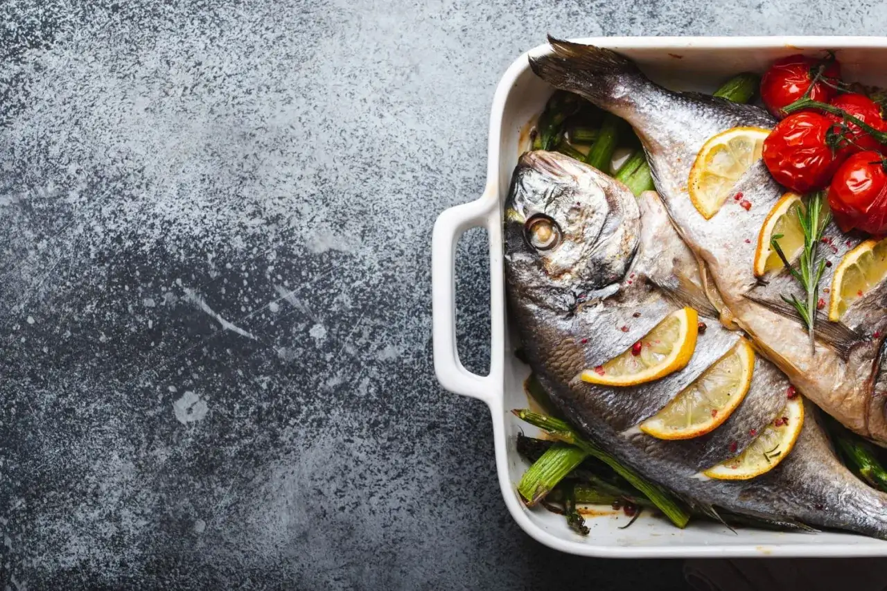 Deux poissons entiers, pr&ecirc;ts pour le temps de cuisson saint-pierre au four, accompagn&eacute;s d'asperges, de tomates cerises et de rondelles de citron.