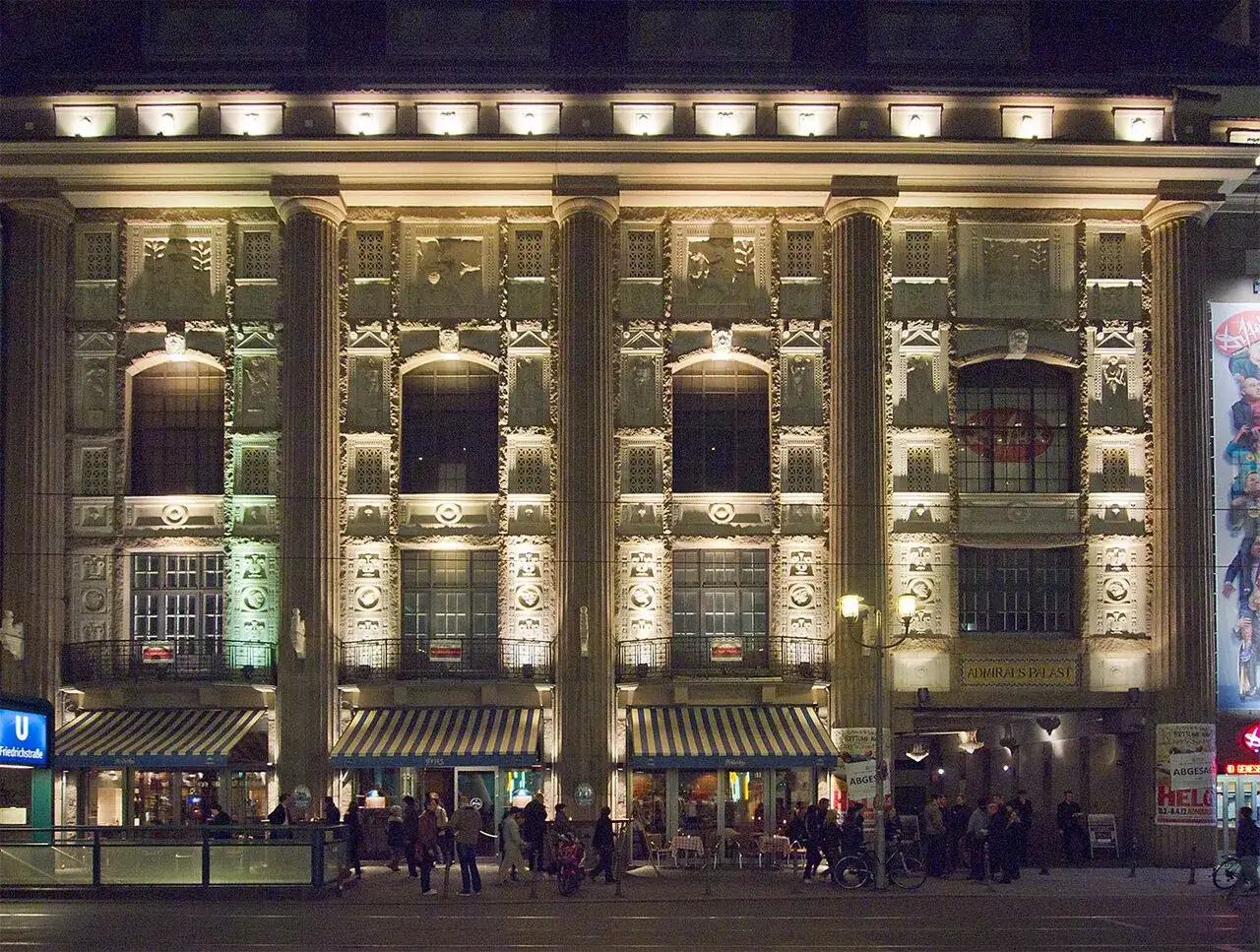 Der Admiralspalast Berlin bei Nacht, beleuchtet mit S&auml;ulen und aufwendiger Fassade. Menschen versammeln sich davor.