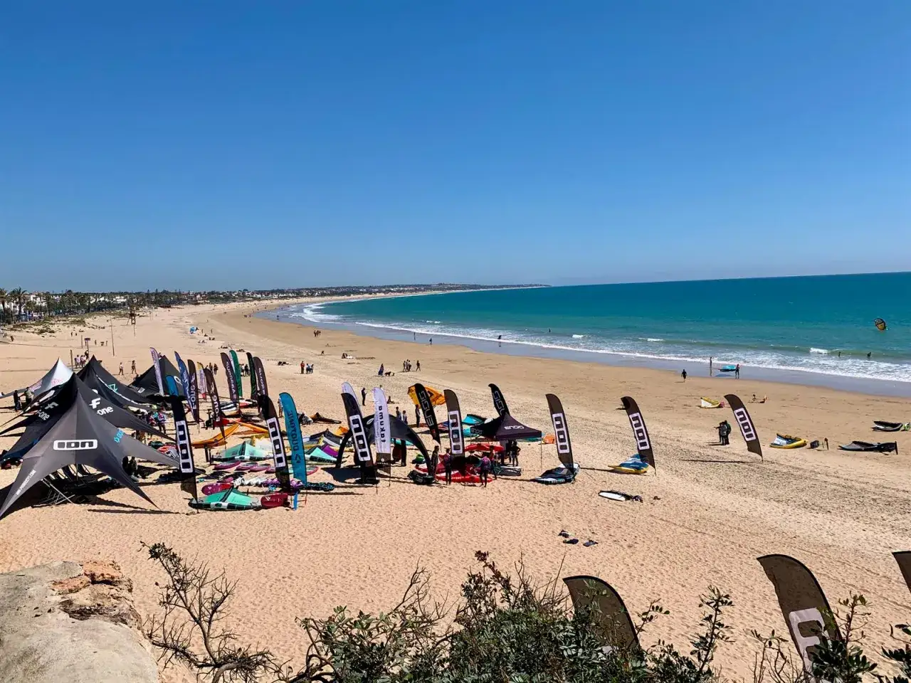 Bunte Kitesurf-Ausr&uuml;stung und Zelte am Chiclana de la Frontera Strand. Menschen genie&szlig;en den sonnigen Tag am Meer.