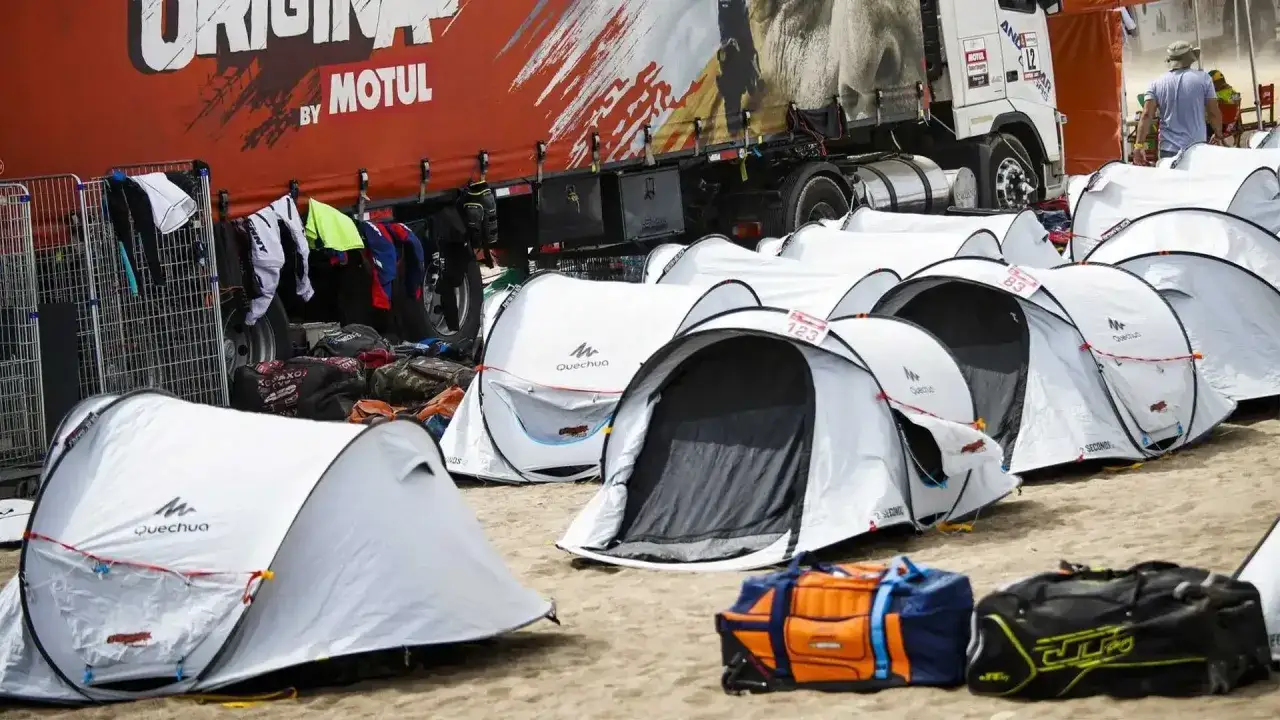 Campement de tentes blanches devant un camion d'assistance Dakar. V&ecirc;tements de course accroch&eacute;s &agrave; une grille.