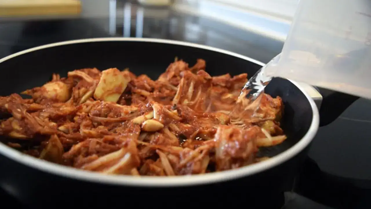 Jackfruit deshebrado en salsa, listo para convertirse en un delicioso pulled pork vegano. Se añade líquido a la sartén.