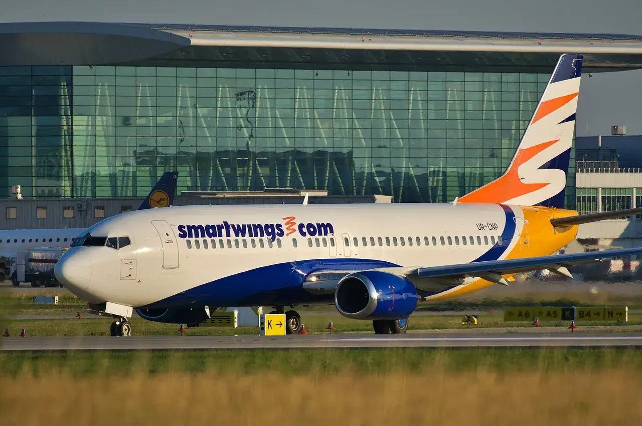 Samolot Smartwings z charakterystycznym logo na ogonie kołuje po płycie lotniska. W tle nowoczesny terminal.
