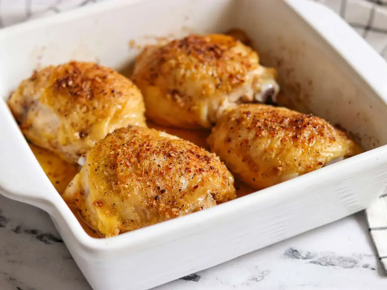 Quatre cuisses de poulet au four, dorées et savoureuses, reposent dans un plat blanc.