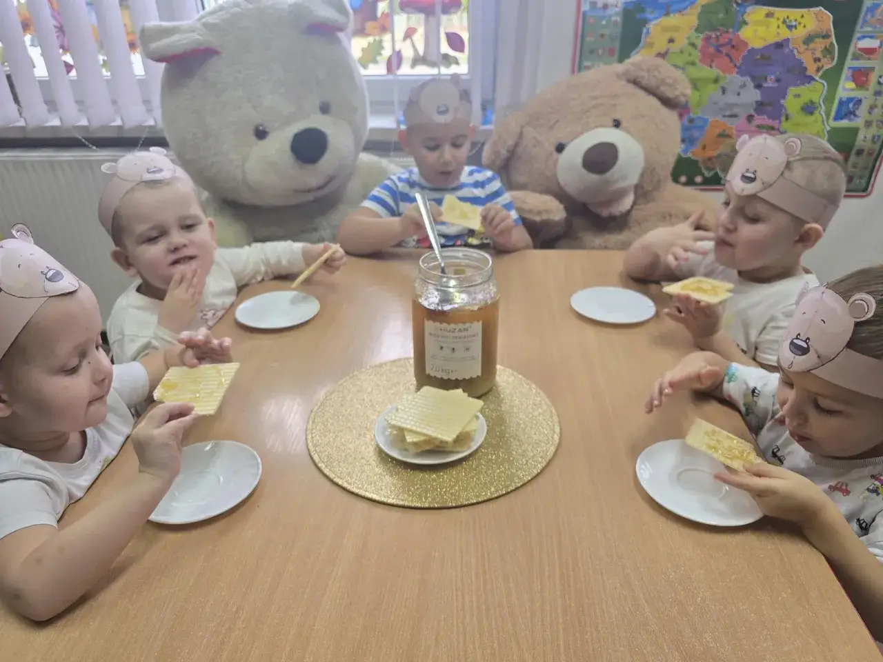 Dzieci w opaskach z uszami misia jedzą wafle z miodem. Mały miś jest głodny i chętnie się częstuje.