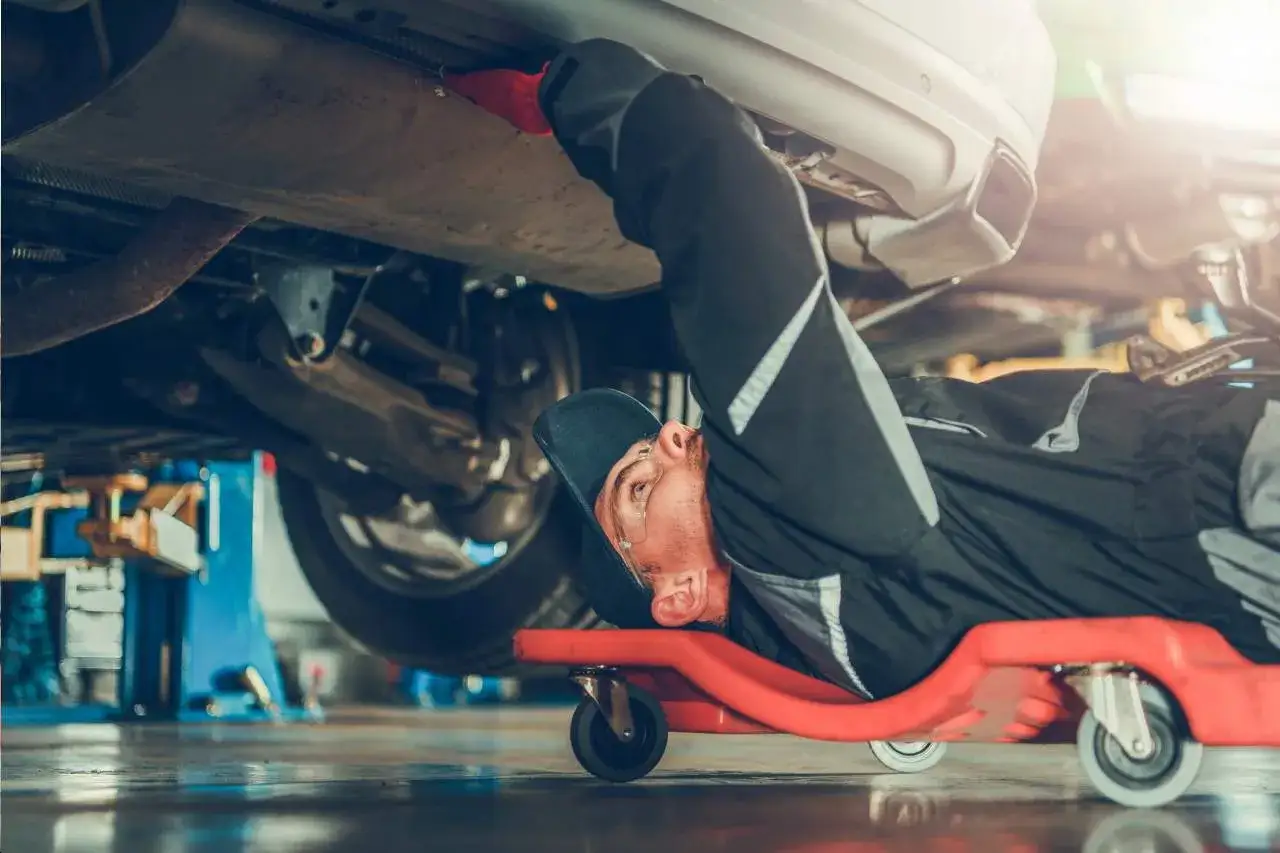 Mechanik w auto complex Adam Woźniak pracuje pod samochodem, leżąc na wózku.
