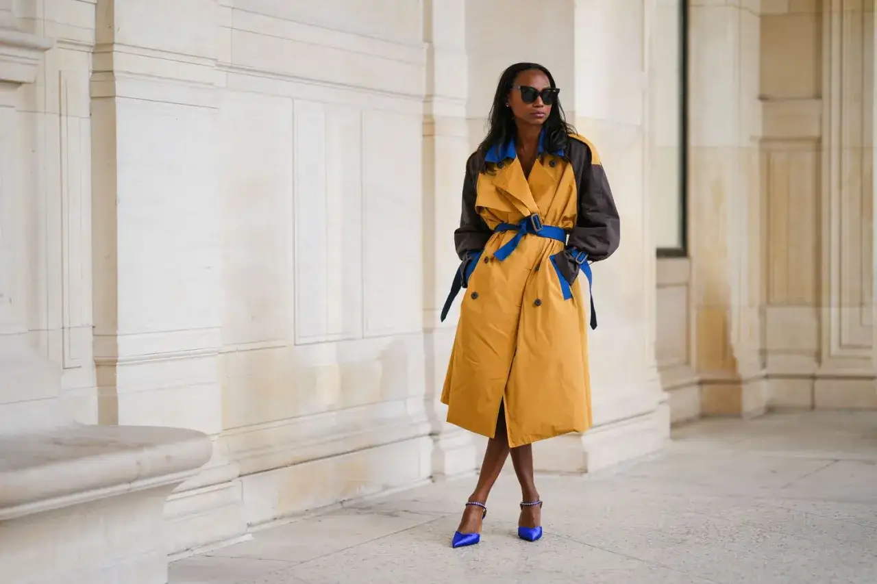 Mujer con gabardina bicolor, amarilla y marrón, con cinturón azul. Un ejemplo de como llevar una gabardina mujer con estilo.