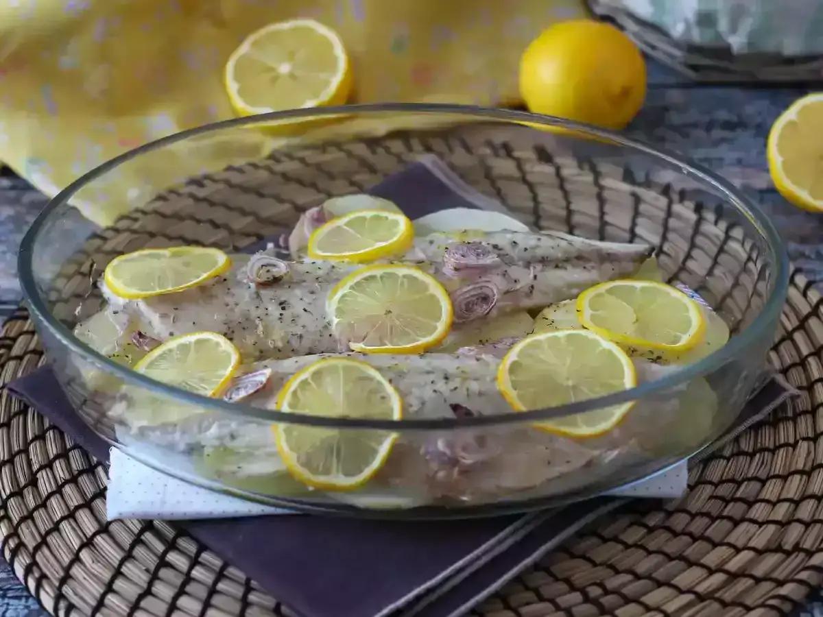 Två hela makrillar förberedda för att bakas i ugnen, toppade med citronskivor och örter.