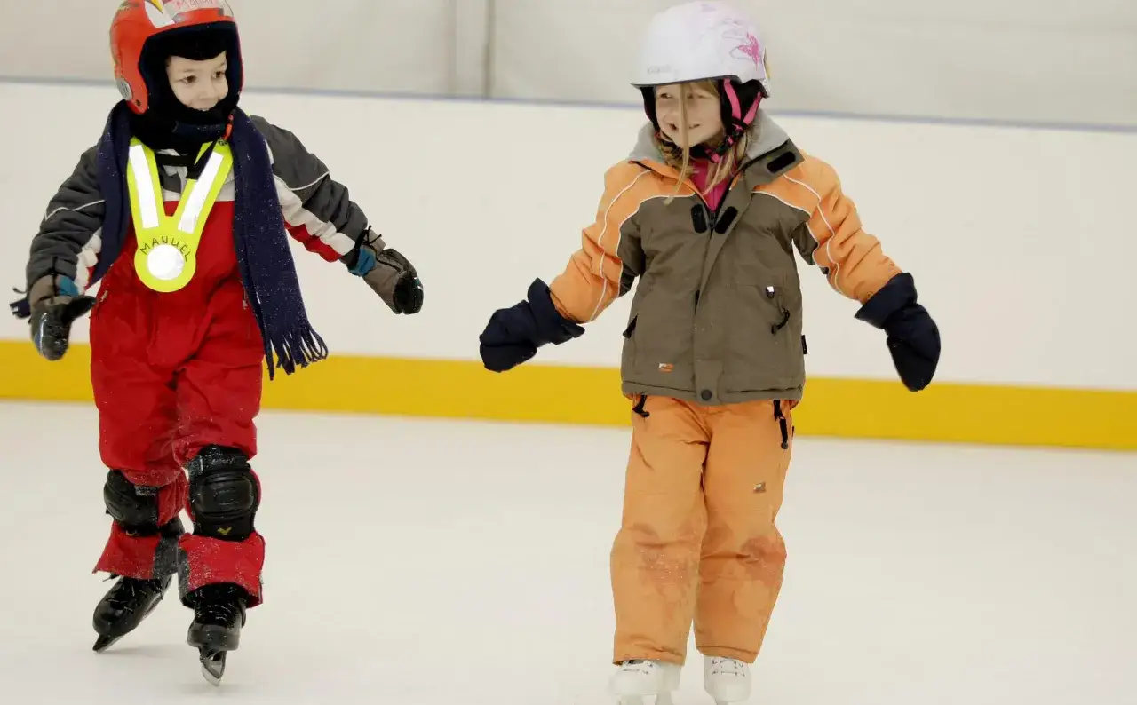Bambini si divertono con il pattinaggio sul ghiaccio, indossando caschi e abbigliamento protettivo.