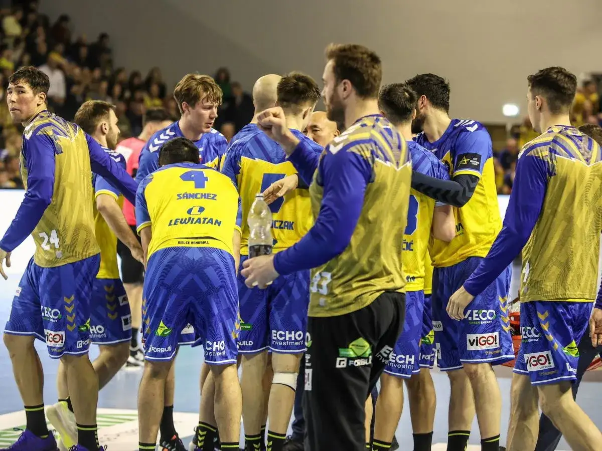 Drużyna Vive Kielce w ż&oacute;łto-niebieskich strojach, zawodnicy rozmawiają między sobą, jeden z nich trzyma butelkę wody.