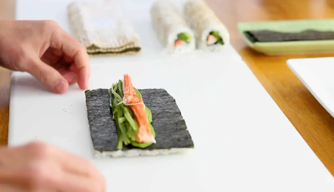 H&auml;nde rollen sushi ohne Matte. Nori, Reis, Gurke und Surimi liegen bereit f&uuml;r die Zubereitung von sushi rollen.