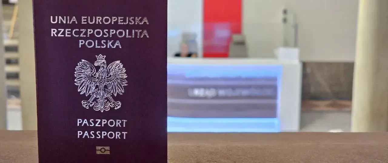 Polski paszport na pierwszym planie. W tle widać fragment lady i osoby, co może sugerować, jak sprawdzić czy paszport jest aktywny.