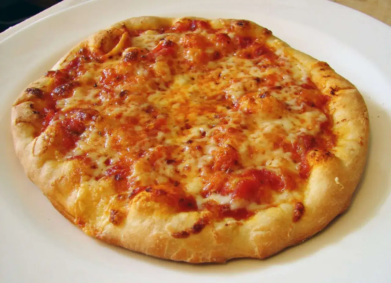 Pyszna, okrągła california pizza z ciągnącym się serem i sosem pomidorowym na białym talerzu.