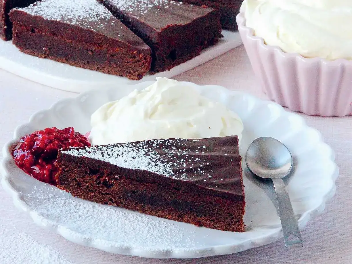 En bit fransk chokladtårta med vispad grädde och hallonsylt. Pudrad med florsocker.