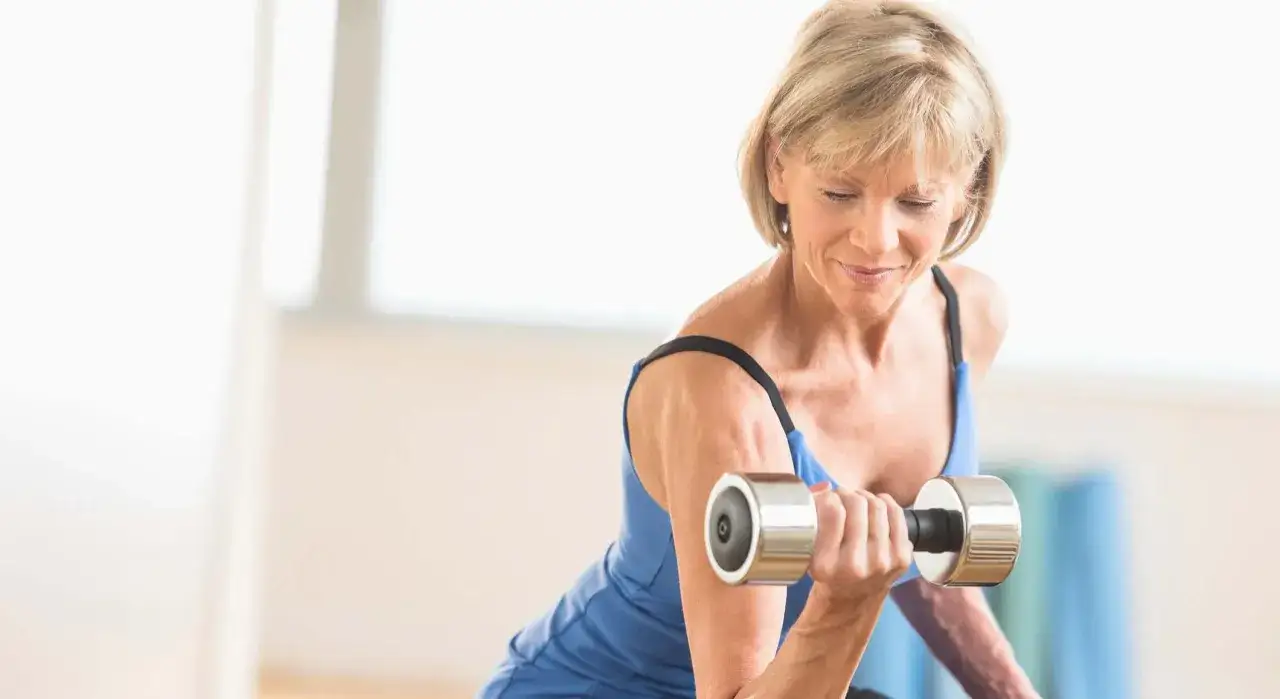 Mujer de 50 a&ntilde;os tonificando brazos con mancuerna.
