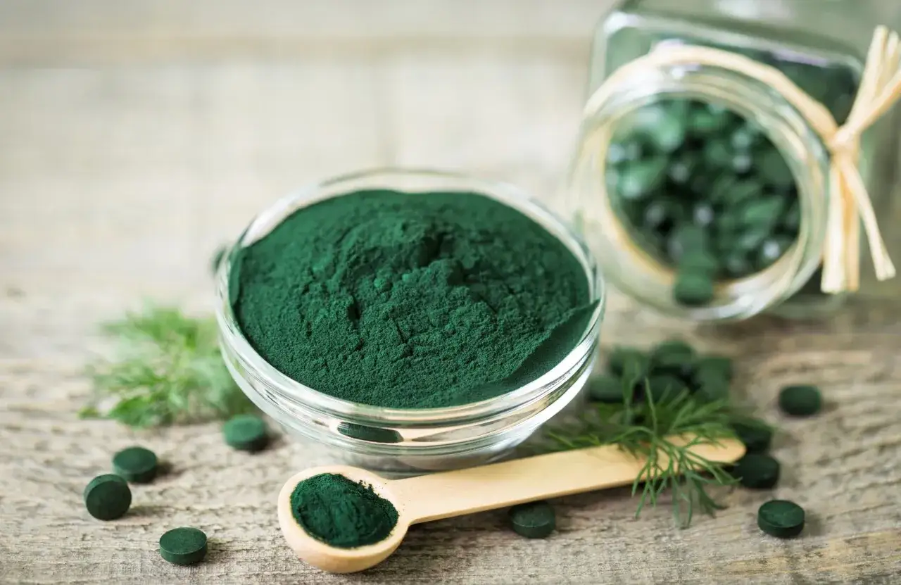 Grön spirulinapulver i skål och kapslar i burk. Tänk på eventuella spirulina biverkningar vid användning.