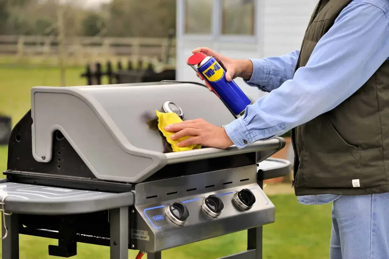 Mann reinigt den Grillrost mit einem Tuch und einer Sprühdose.