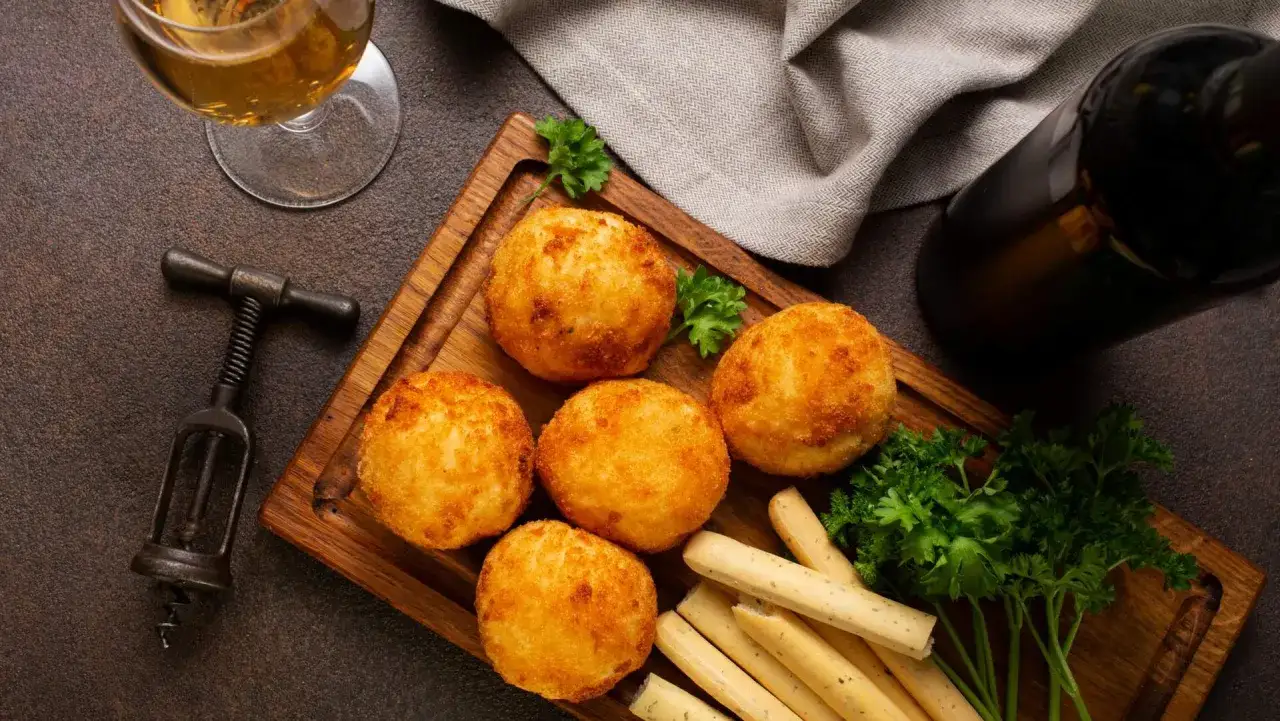 Goldbraune polpette di patate auf Holzbrett, garniert mit Petersilie. Daneben ein Weinglas, Flasche und Korkenzieher.