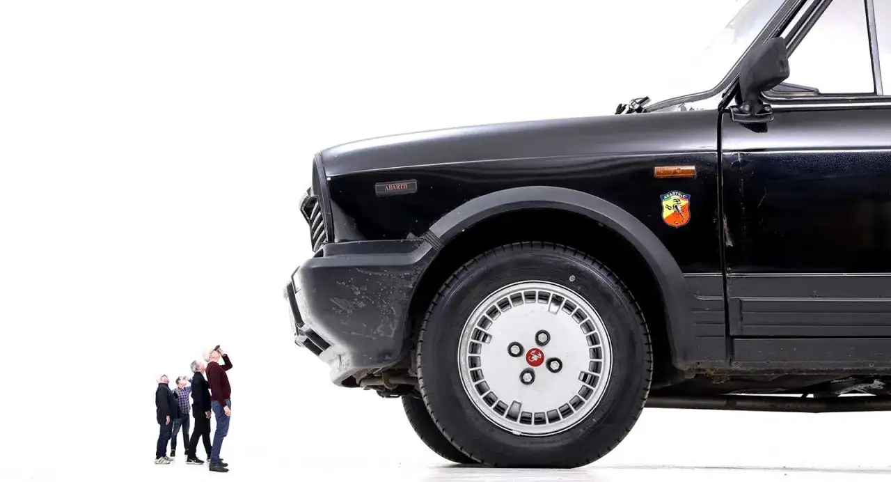 En grupp m&auml;n tittar upp mot en svart Lancia A112 Junior.