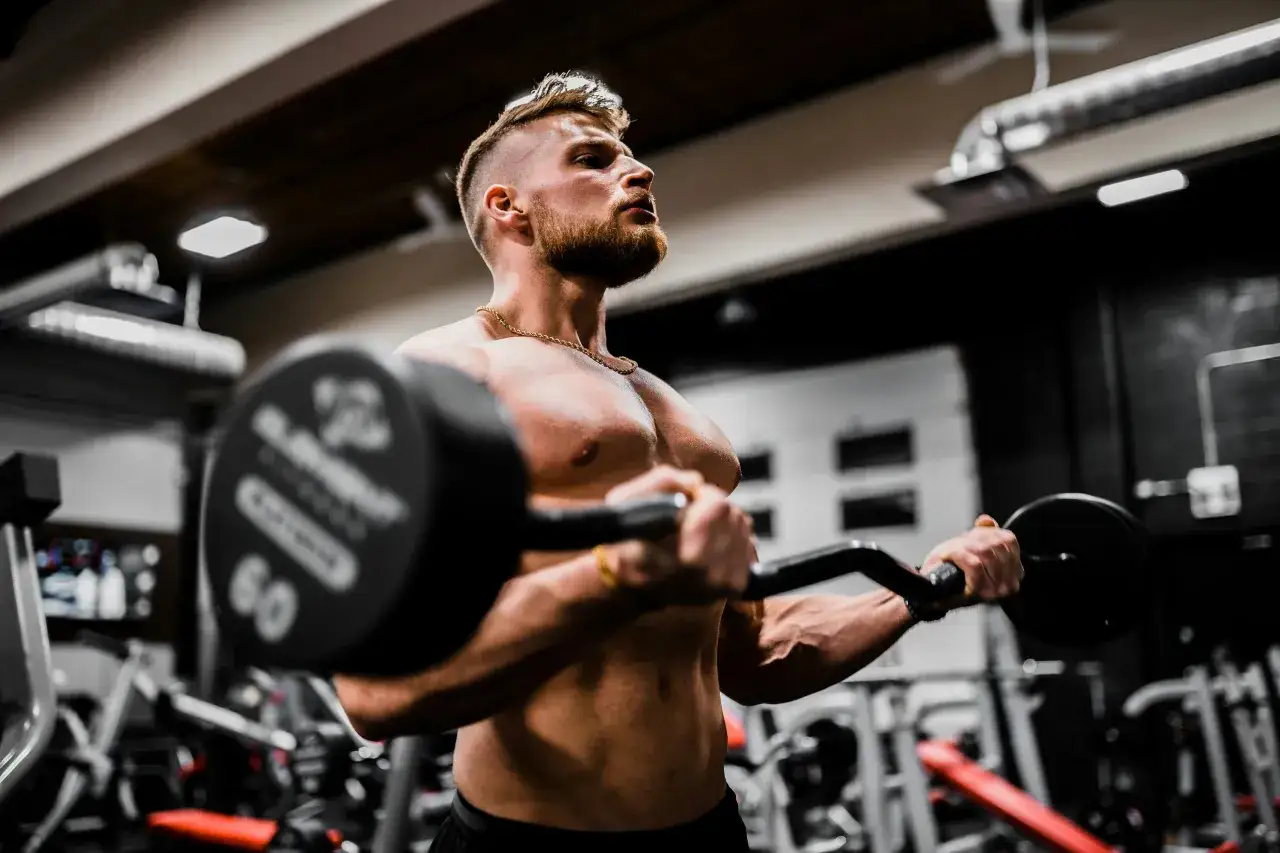 En muskulös man lyfter en skivstång i ett gym. Han fokuserar på träningen, en viktig del av hur blir man stark.