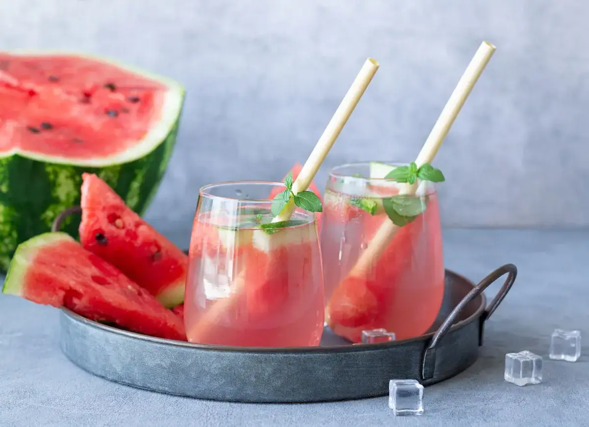 Letnie drinki z wódką w arbuzie – idealny pomysł na orzeźwiającą imprezę. Dwa szklane kieliszki z różowym napojem, kawałkami arbuza i miętą, na tacy z arbuzem i plasterkami owocu.