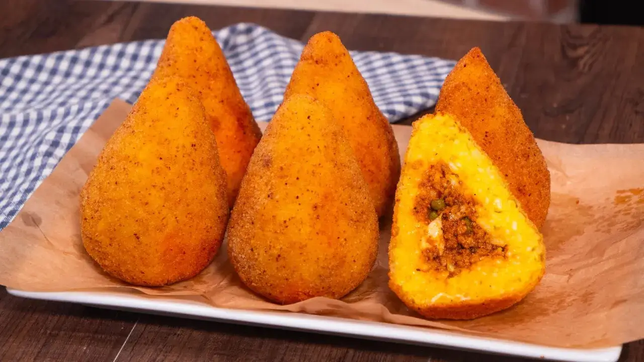 Cinque arancini di riso dorati e croccanti, uno tagliato a met&agrave; rivela un ripieno saporito.