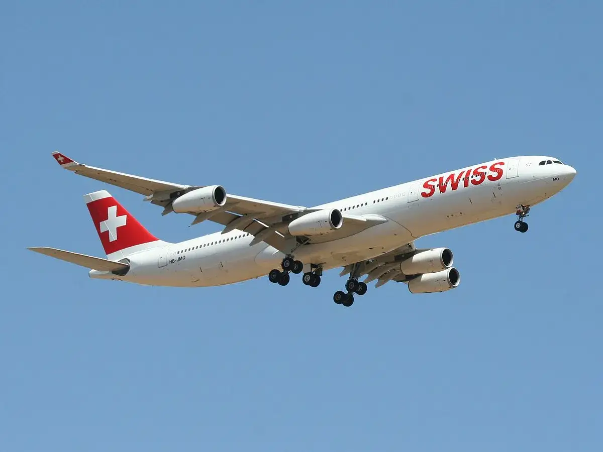 Airbus A340-300 linii Swiss z charakterystycznym czerwonym krzyżem na ogonie wznosi się na błękitne niebo.