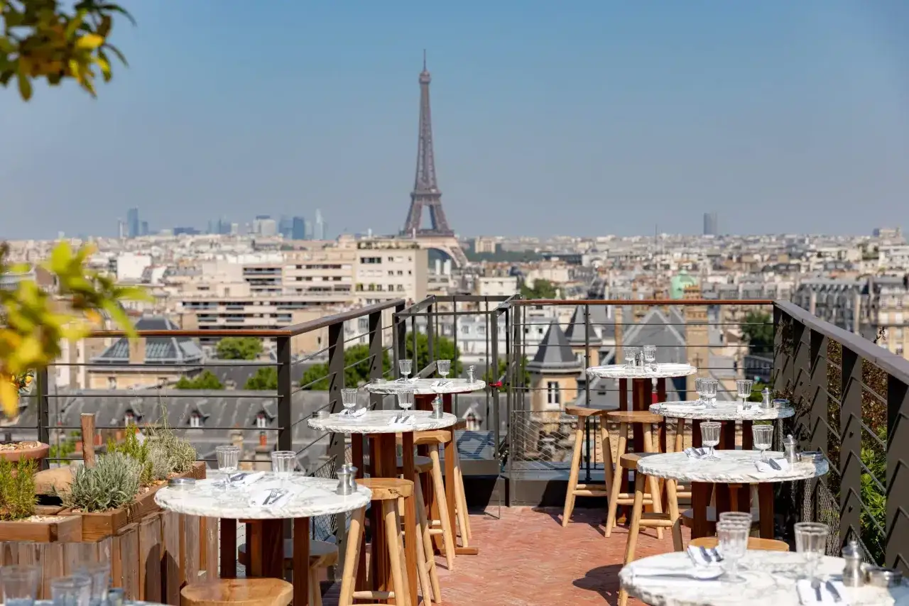 Terrasse avec vue sur Paris, tables dressées et la Tour Eiffel en arrière-plan. Un perchoir porte de Versailles idéal pour un dîner romantique.